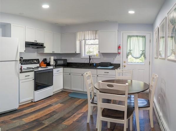 A compact kitchen with white cabinets, a stove, microwave, and a dining area with a table and chairs.