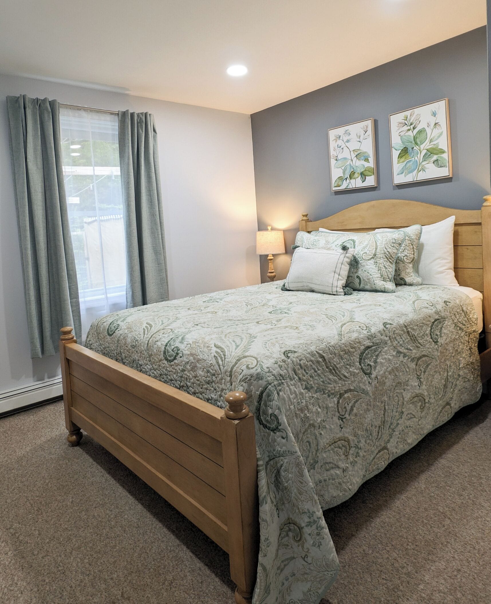 A bedroom with a wooden bed, grey curtains, a bedside lamp, and two floral wall art pieces.