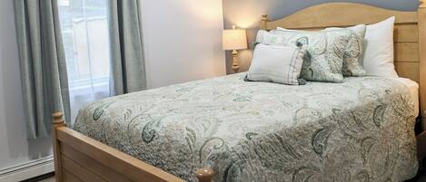 A bedroom with a wooden bed, grey curtains, a bedside lamp, and two floral wall art pieces.