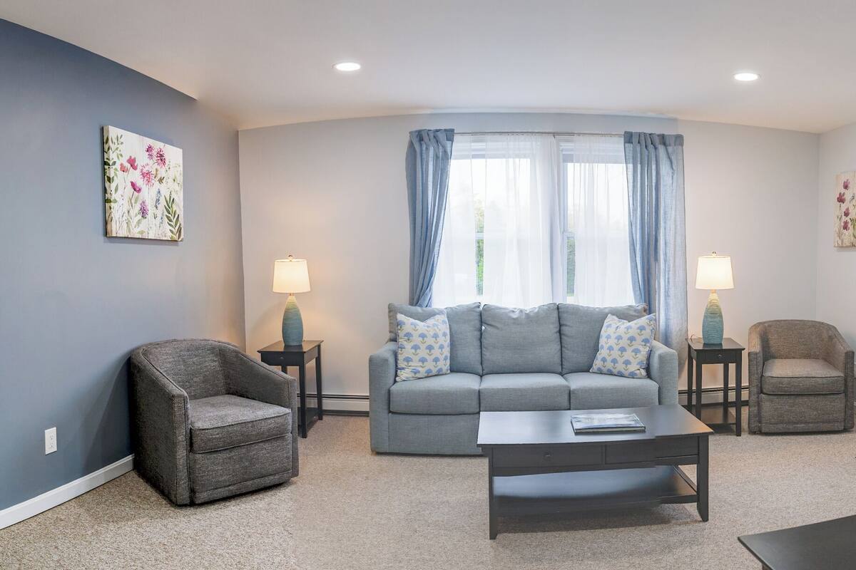 A living room with a grey sofa, two armchairs, a coffee table, and two side tables with lamps.