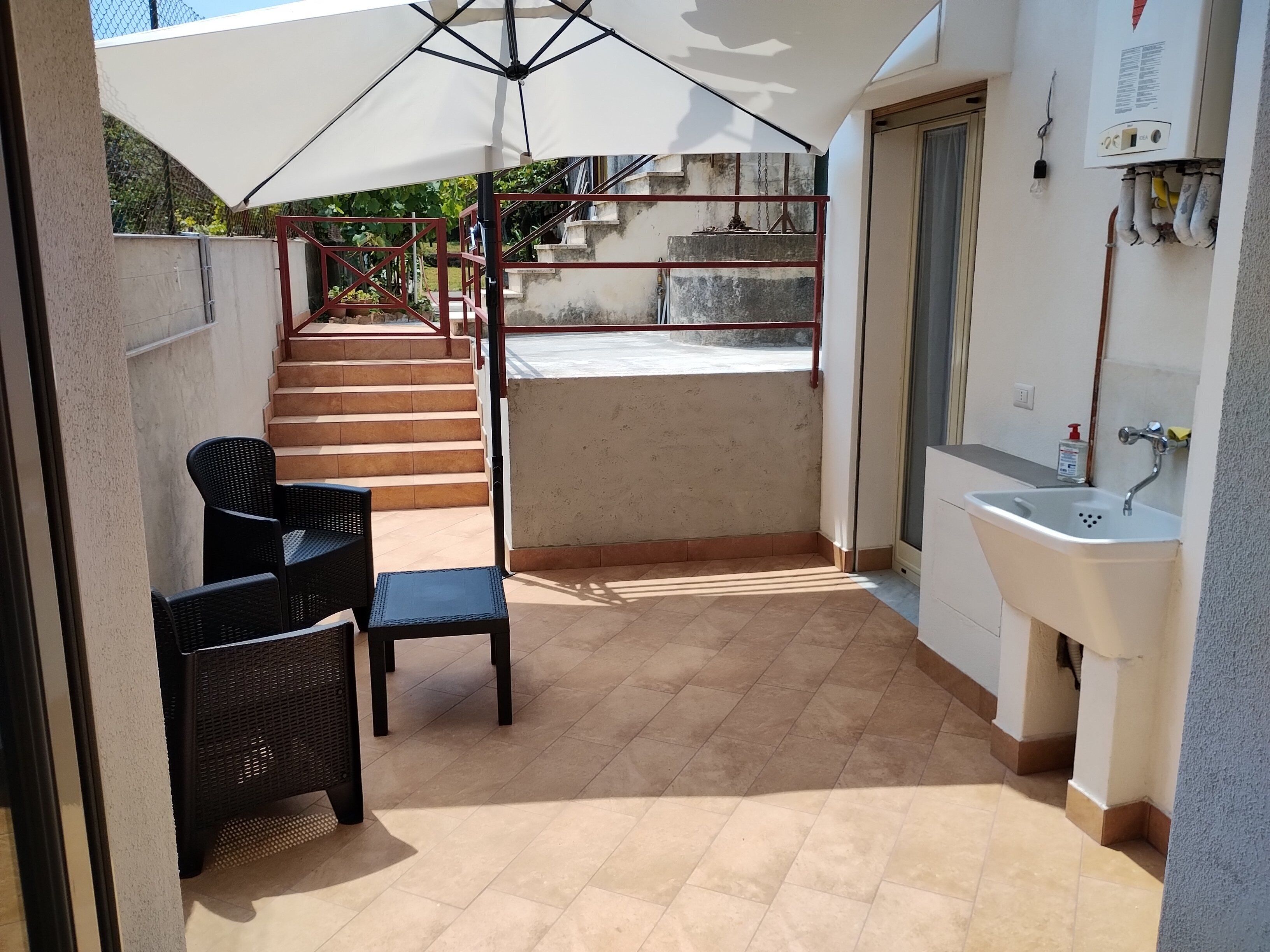 Ein überdachter Außenbereich mit Terrasse, Spüle und einer Treppe zu einem Balkon.
