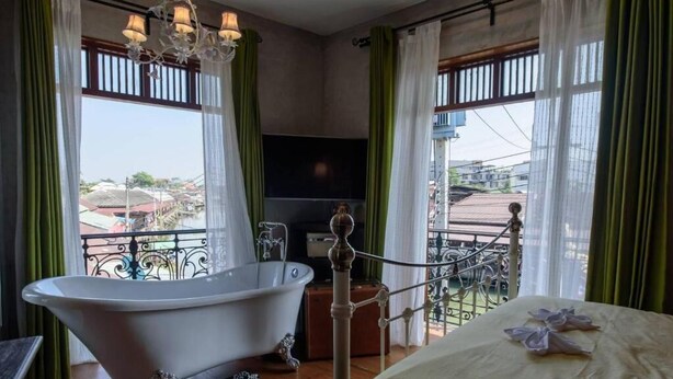 Habitación con bañera, cama, televisión y balcón con vistas a edificios.