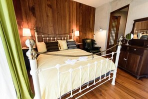 A bedroom with a wooden headboard, a white metal bed frame, two bedside lamps, a black chair, and a wooden wardrobe. - Roomquest Rimrabeang Amphawa Floating Market (Amphawa)