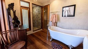 Un baño con una bañera independiente, una silla de madera, un espejo y un cuadro en la pared.
