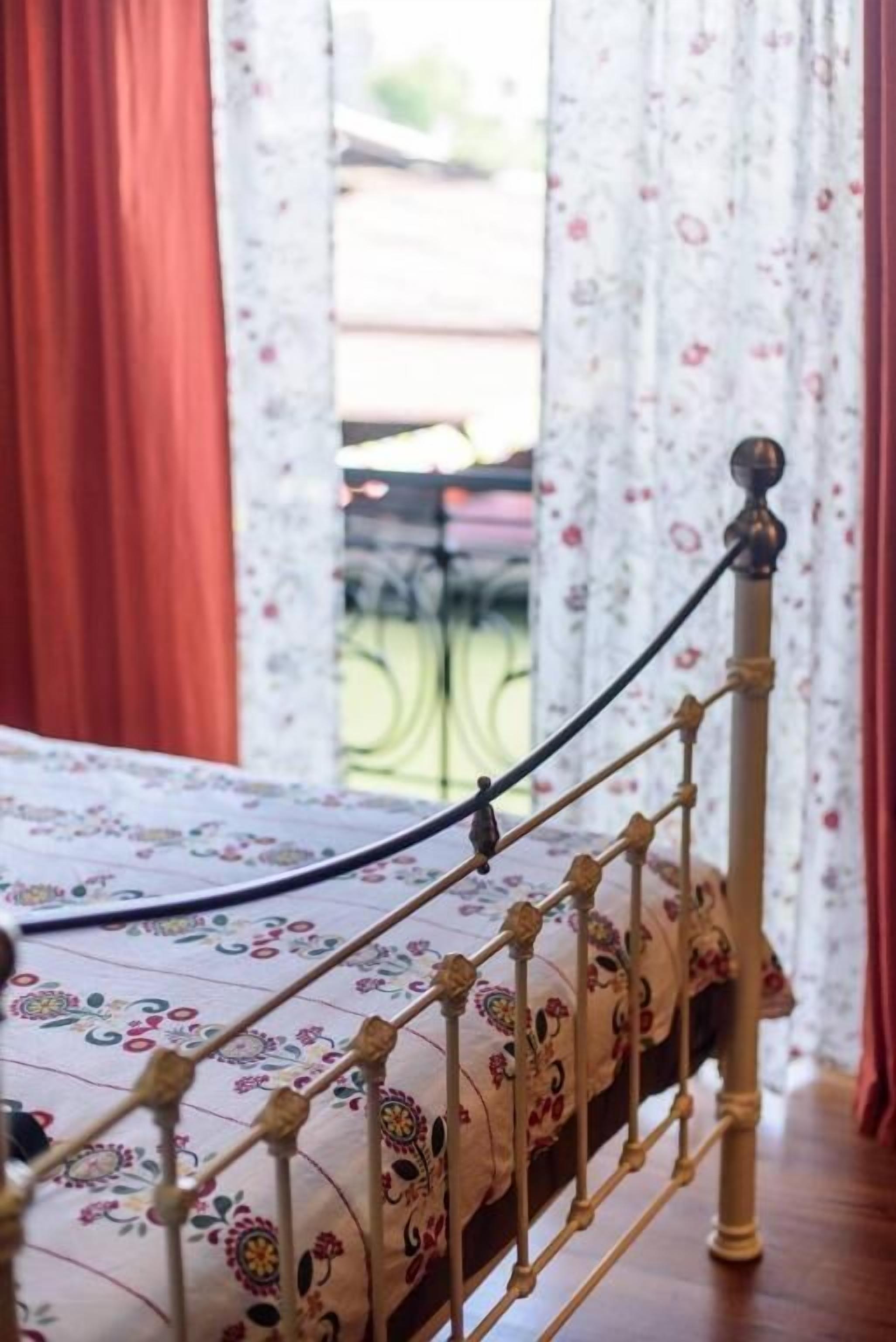 Un letto con una coperta a fiori, una testiera in metallo e vista su un balcone con ringhiera.