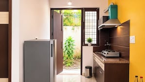 Cocina compacta con refrigerador, estufa y armarios, que da a una puerta con vista a un jardín.