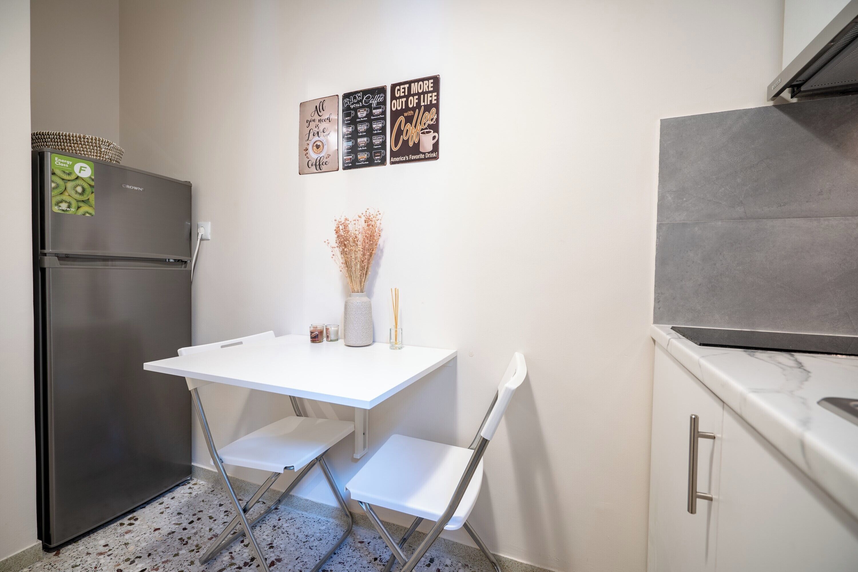Una cuina compacta amb nevera, taula blanca i caires, i decoracions murals.