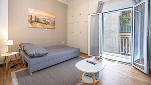 Un dormitorio compacto con una cama individual, una mesita pequeña, un cuadro colgado en la pared y una puerta corrediza de vidrio que da a un balcón.