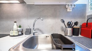 Cocina moderna con pileta de acero inoxidable, contenedor de basura integrado y electrodoméstico rojo.