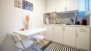 Una cocina compacta con armarios blancos, una mesa de comedor blanca con dos sillas, y una alfombra a rayas.