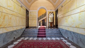 A grand hallway with marble walls, a red carpeted staircase, and a checkered floor. - Amari Elegant Apartment by Wonderful Italy (Palermo)