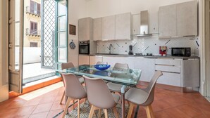 A modern kitchen with a glass dining table, chairs, and a view of the street through an open door. - Amari Elegant Apartment by Wonderful Italy (Palermo)