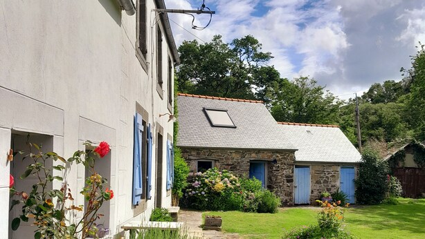 A white building with blue shutters, a stone house with a tiled roof, and a well-maintained garden with various plants and flowers. - Beautiful country house at the entrance to the Crozon peninsula (Rosnoën)