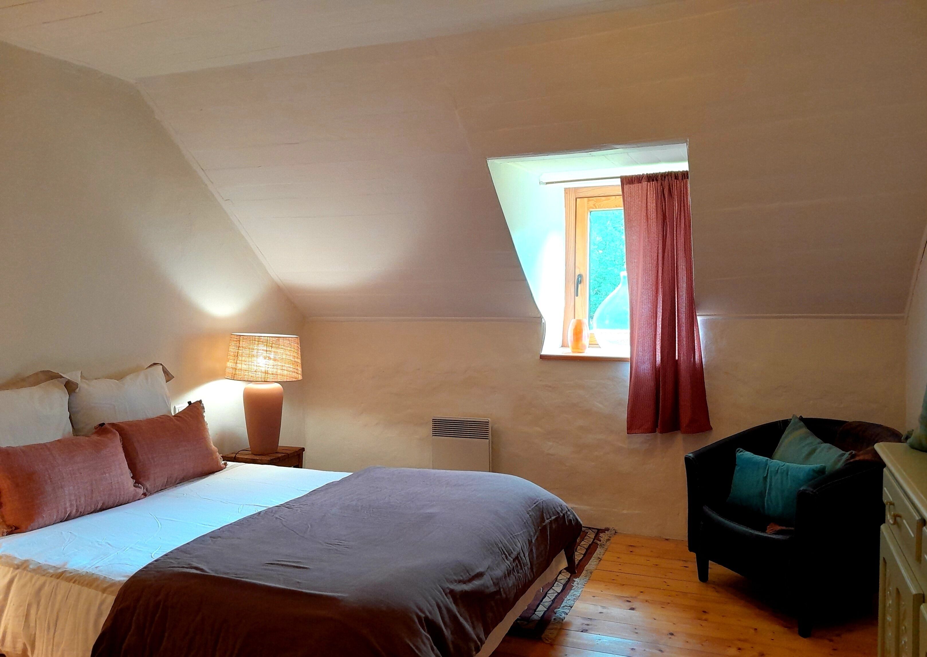 A bedroom with a bed, a chair, a lamp, and a window with curtains.