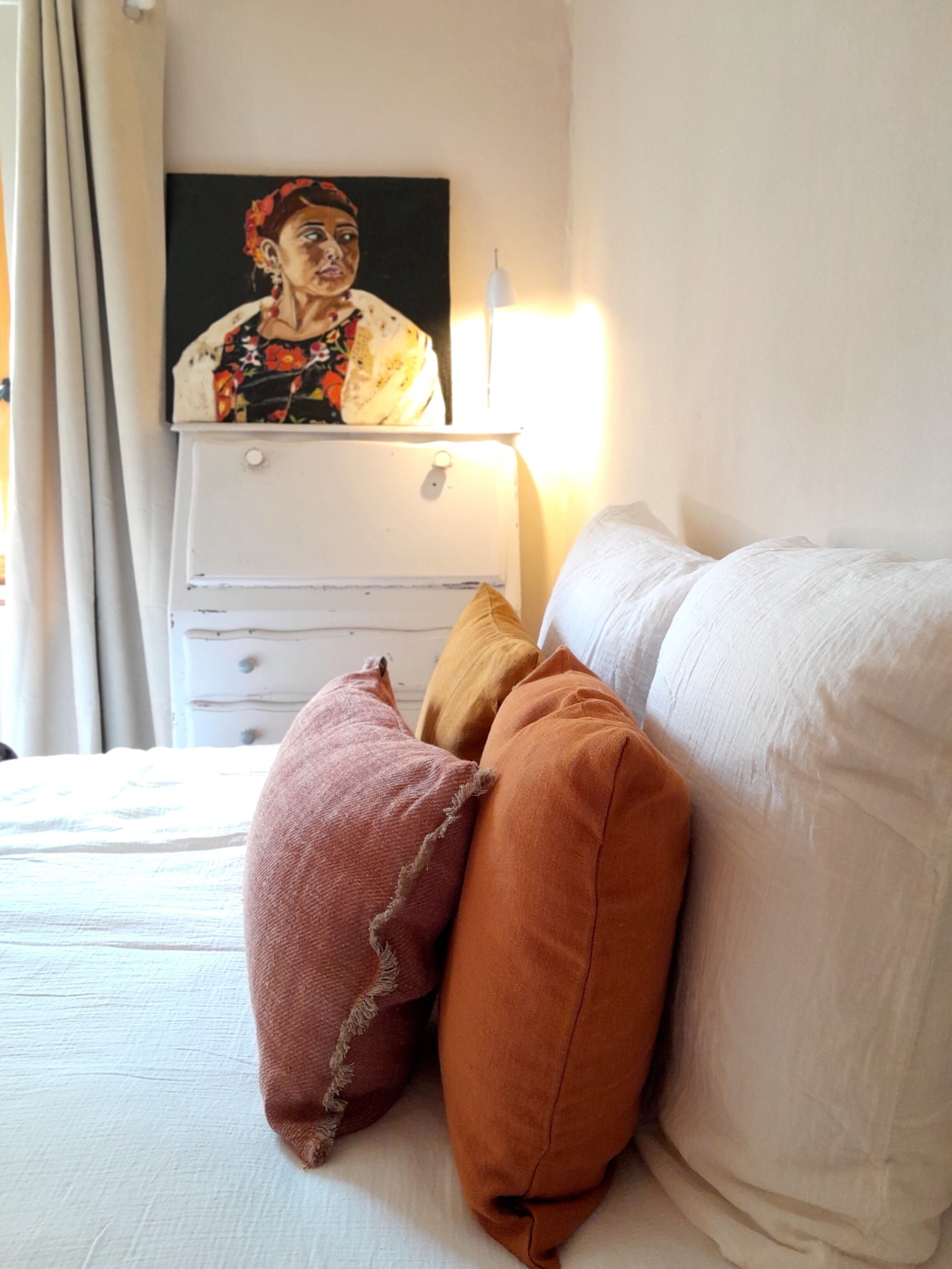 A bedroom with a bed, pillows, a dresser, and a painting on the wall.