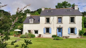 A two-story house with a well-maintained lawn, a patio with a table and chairs, and a blue door. - Beautiful country house at the entrance to the Crozon peninsula (Rosnoën)
