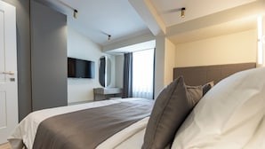 Une chambre d’hôtel moderne dotée d’un grand lit, d’un téléviseur à écran plat fixé au mur et d’une fenêtre avec des rideaux.