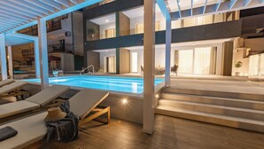 Un espace piscine intérieur moderne, doté de chaises longues, d’un escalier et offrant une vue sur l’étage supérieur.