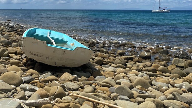 Un bateau sur une plage rocheuse, avec un voilier visible au loin.