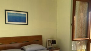 Une chambre à coucher avec un lit, une table de chevet, une lampe, un tableau encadré et une fenêtre avec des rideaux.