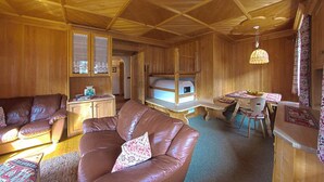 Un acogedor interior de cabaña con techo de madera, una zona de comedor, un sofá y un televisor.