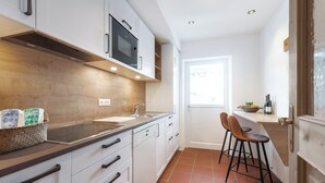 Una cocina moderna con armarios blancos, encimera de madera, microondas integrado y una ventana que proporciona luz natural.