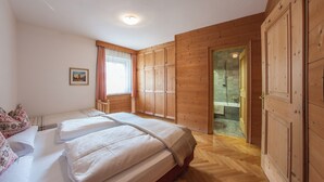 Un dormitorio con dos camas, paredes de madera, una ventana con cortinas y un baño visible a través de una puerta de cristal.