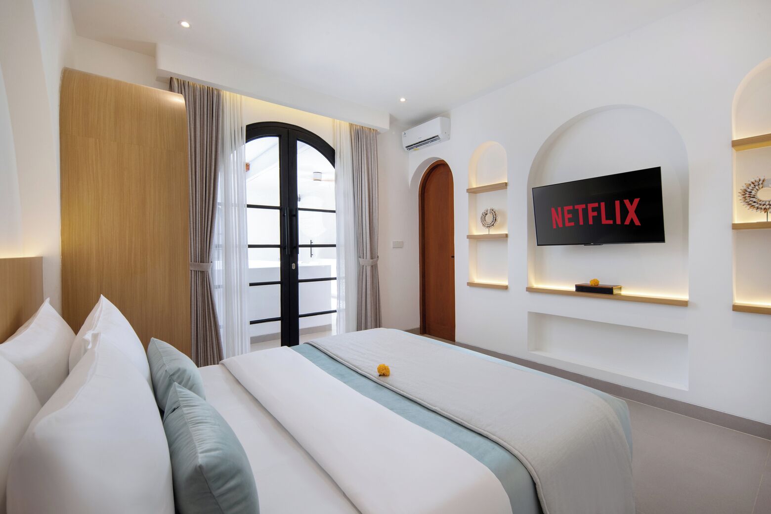 Habitación de hotel con una cama, televisor montado en la pared y ventana con cortinas.