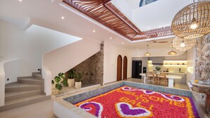 A modern interior with a central decorative flower arrangement, a staircase, and a kitchen area. - Onnea Villa by Lead (Canggu)