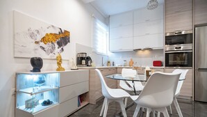 A modern kitchen with white cabinetry, a glass dining table, and white chairs. - Neo Irakleio train st 1 bedrm 4 pers apartment by MPS (Iraklio)