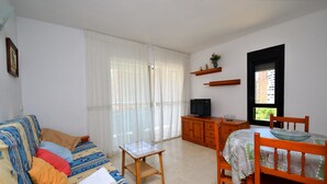 A living room with a sofa, a small table, a dining table with chairs, a television, and a window with curtains. - PARQUE EUROPA (1 BEDROOM) (Benidorm)