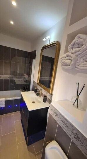 Bathroom features a central sink area, bathtub, and large mirror with a gold frame.