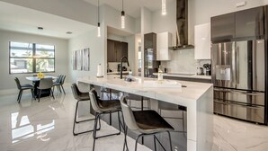 A modern kitchen with a large island, bar stools, and a stainless steel refrigerator. - Villa Suntastic - gulf access, pool & spa (Cape Coral)