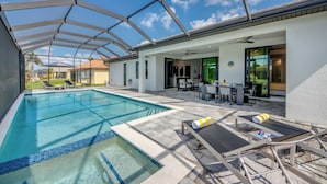 A swimming pool with a glass ceiling, lounge chairs, and a patio area with outdoor furniture. - Villa Suntastic - gulf access, pool & spa (Cape Coral)
