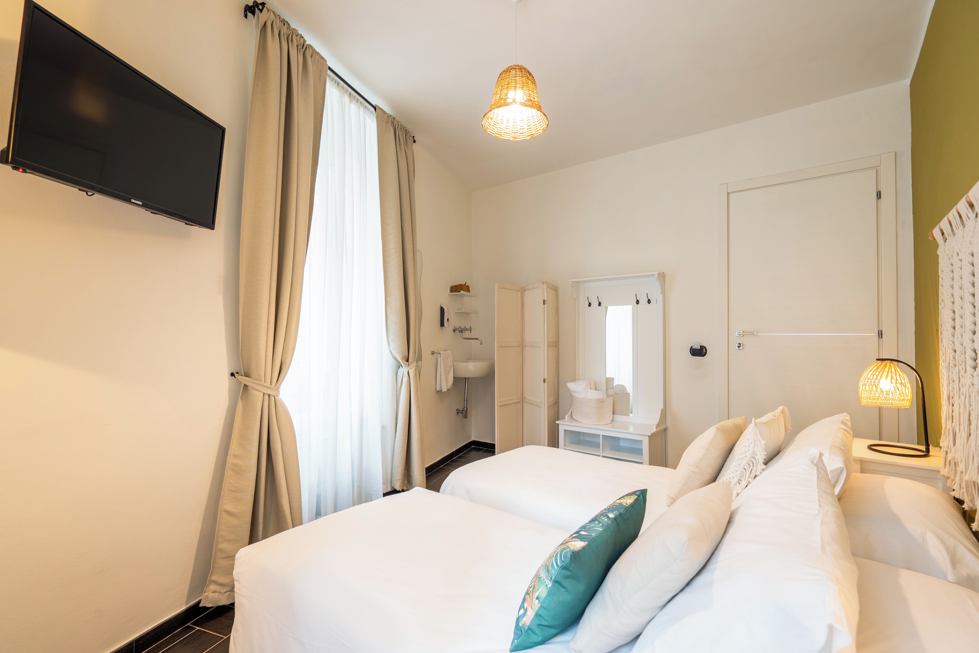 A hotel room with two beds, a TV, a sink, and a mirror.