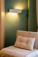A room with a green wall, a white light fixture, and a beige sofa with a matching pillow.