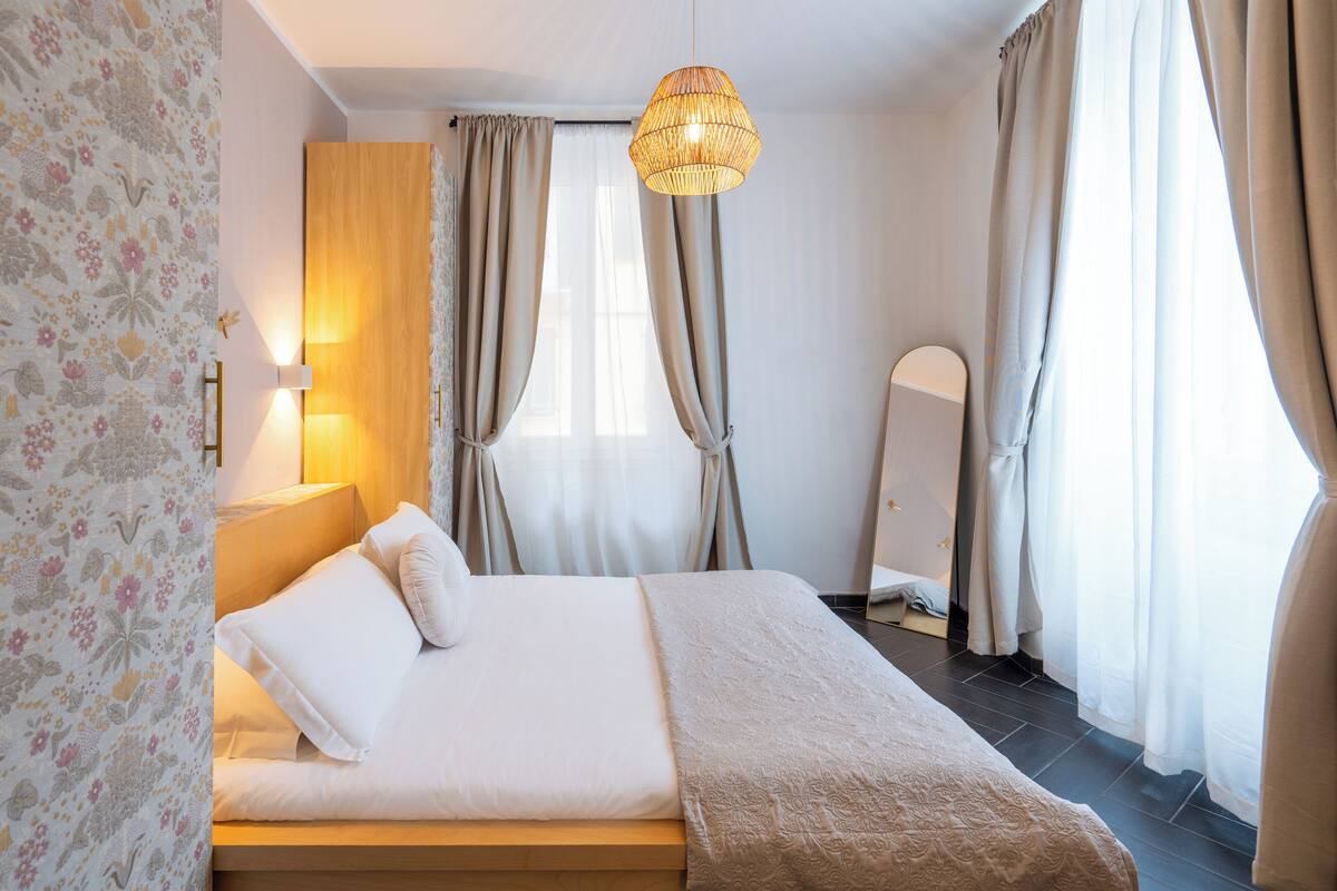 Ein ordentlich bezogenes Bett mit Kopfteil, einer Nachttischlampe und einer Deckenleuchte.