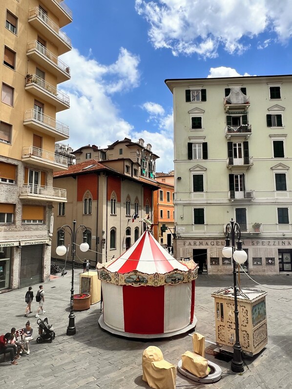 Uma praça italiana tradicional com uma tenda listrada em vermelho e branco, pavimento de paralelepípedos e edifícios históricos com sacadas.