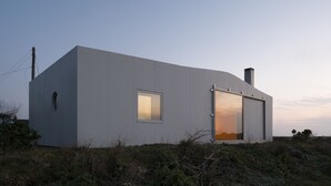 Een modern, gelijkvloers gebouw met een grote schuindeur en een klein raam.