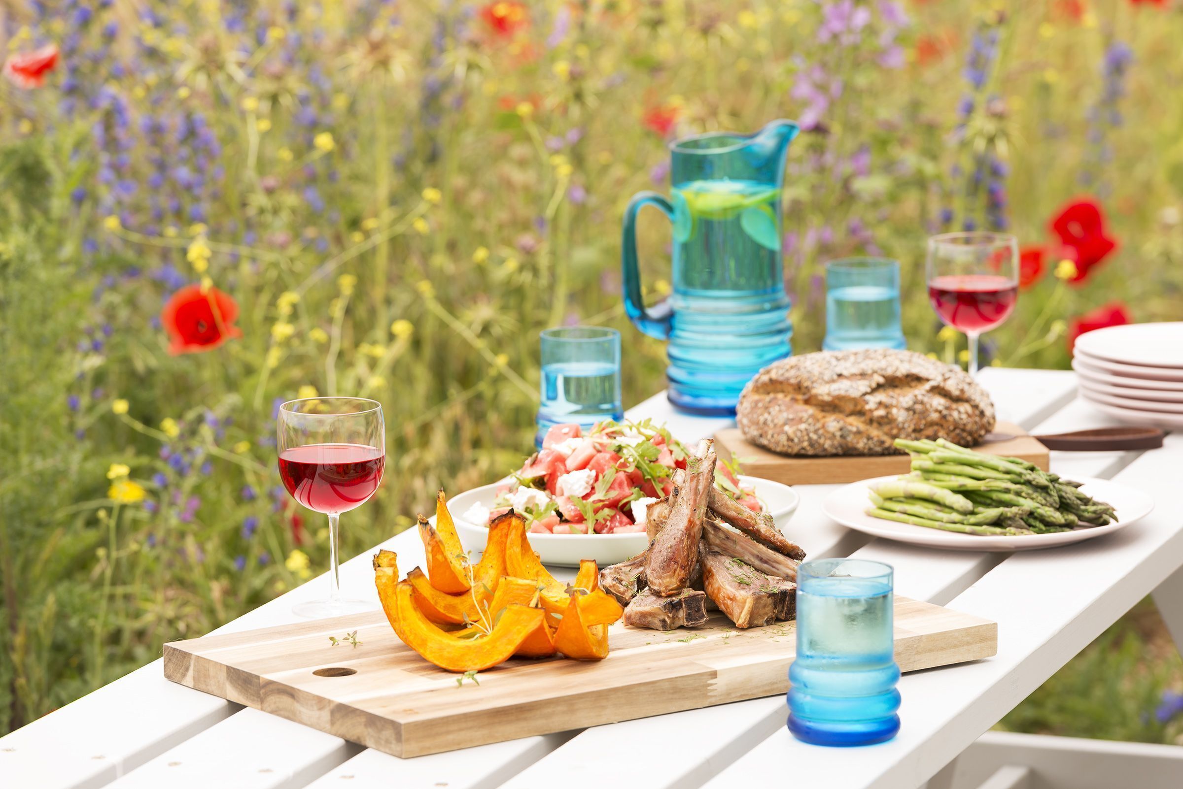 Ein Picknick mit Essen und Getränken auf einem Holztisch, umgeben von einem Blumenfeld.