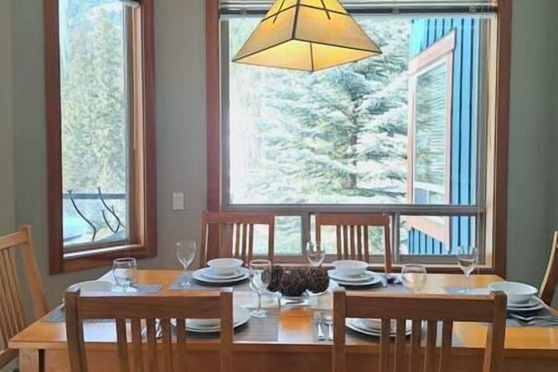 A dining table set for four with chairs, a chandelier, and a view of trees through a window.