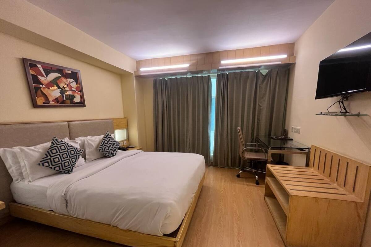 Una habitación de hotel con una cama, un escritorio, una silla, un televisor y un cuadro en la pared.