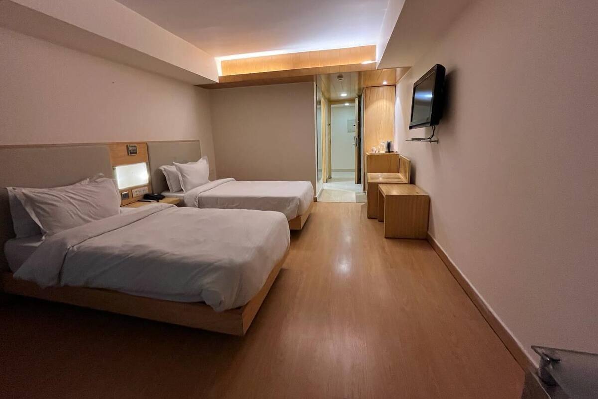Una habitación de hotel moderna con dos camas, un televisor, una mesita de noche y un pequeño escritorio.