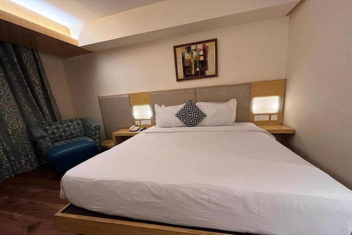 Habitación de hotel con una cama grande, dos mesitas de noche, una silla y una obra de arte colgada en la pared.