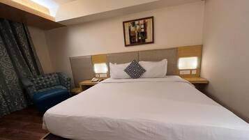 Ein Hotelzimmer mit einem großen Bett, zwei Nachttischen, einem Sessel und einem Wandbild.