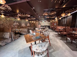 L’intérieur d’un restaurant présente des tables en bois et des chaises à motifs, des murs en pierre et des luminaires décoratifs au plafond.