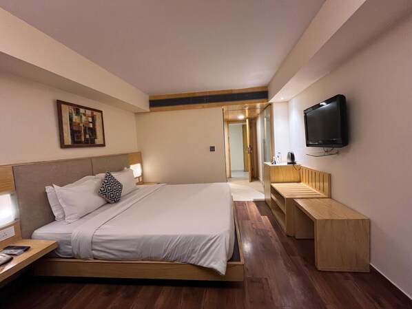 Une chambre d’hôtel moderne avec un grand lit, des tables de chevet, une télévision et un banc en bois.