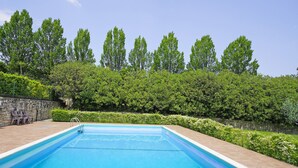 Une piscine rectangulaire à l’eau d’un bleu limpide, entourée d’une terrasse en briques et d’un mur en pierre.