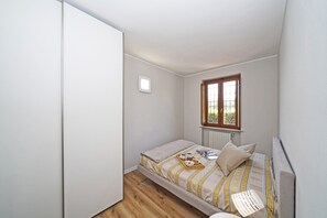 A small, single-bed room with a wooden floor, a window with a view, and a radiator. - Casa Monte Cicogna PT-1 by Wonderful Italy (Moniga del Garda)