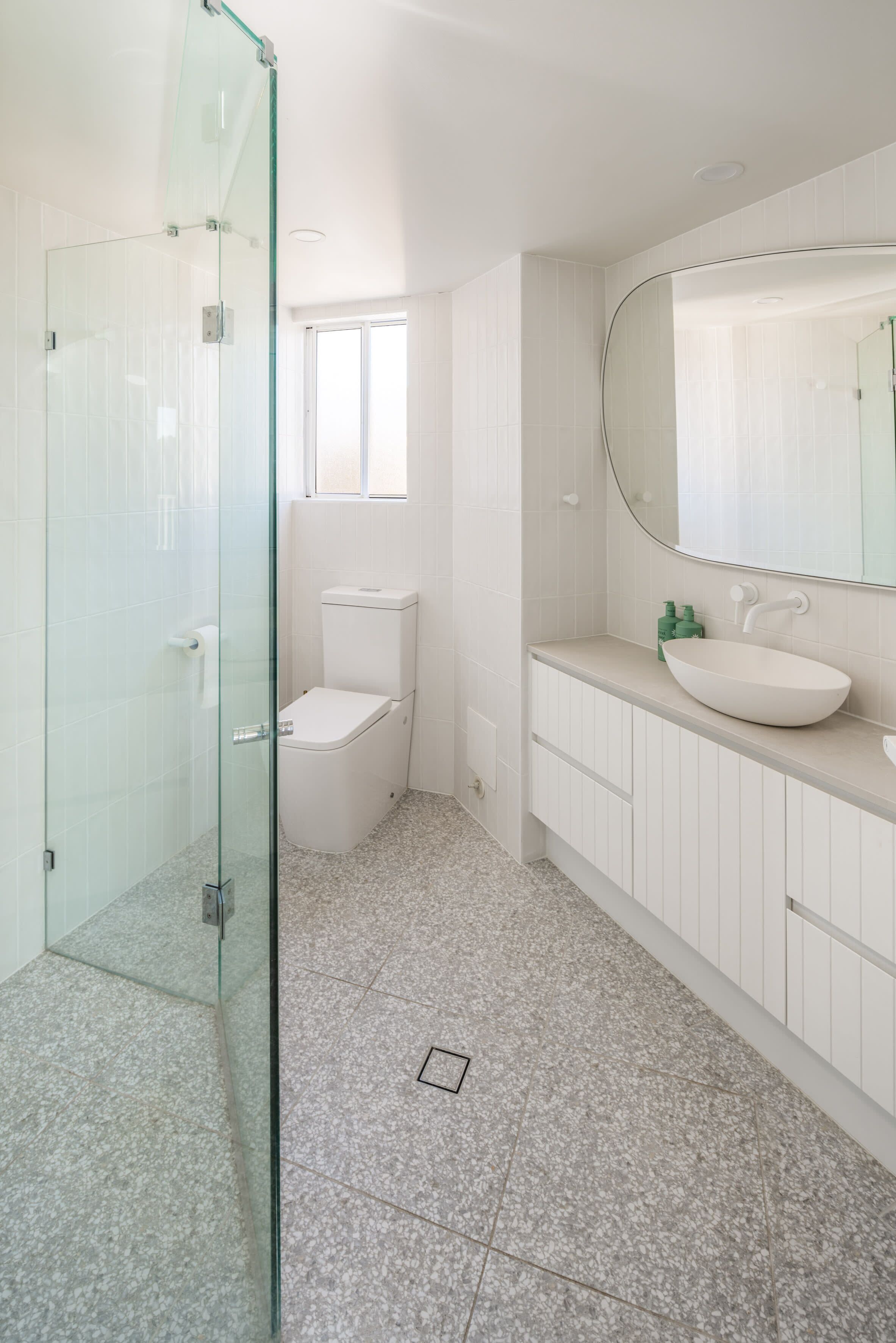 A bathroom with a glass shower enclosure, a toilet, a sink with a mirror, and a window.